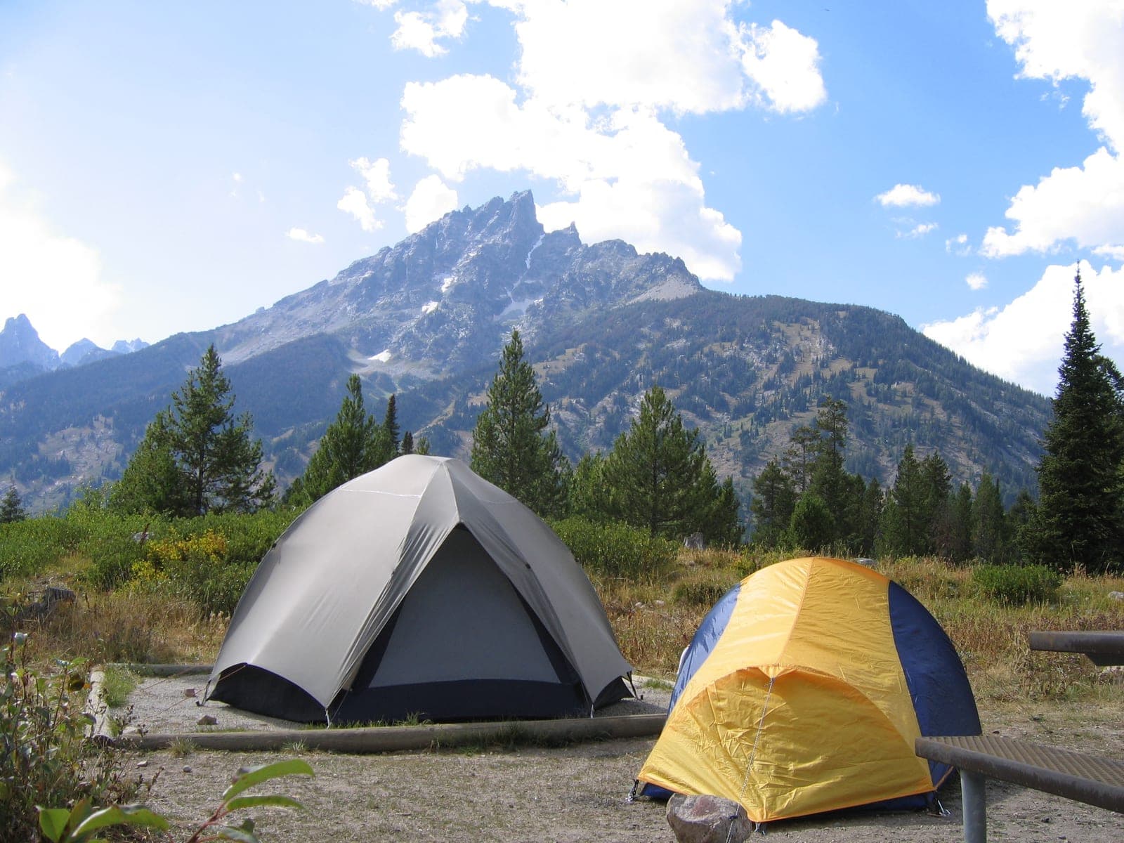 Two tents pitched on a gravel campsite pad below a jagged granite peak