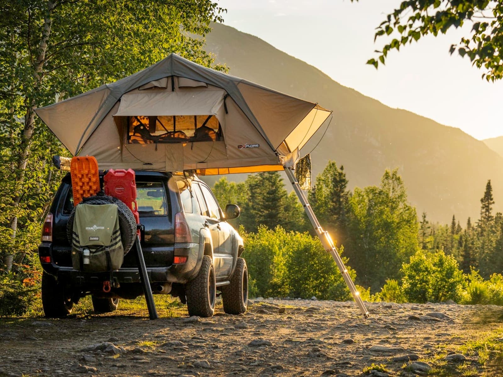 A rooftop tent open on a parked vehicle at a forest campsite in golden evening light