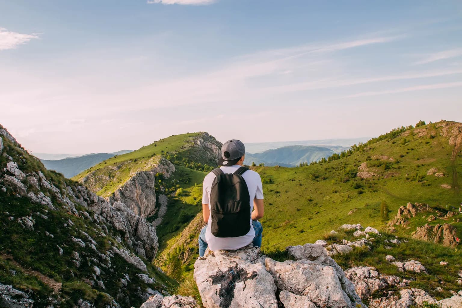 Hiker sitting on a rocky overlook above a green mountain valley