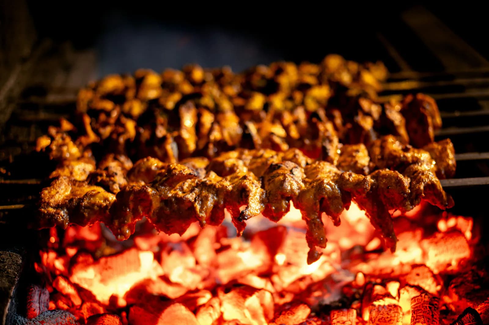 Meat skewers cooking above a bright bed of glowing coals
