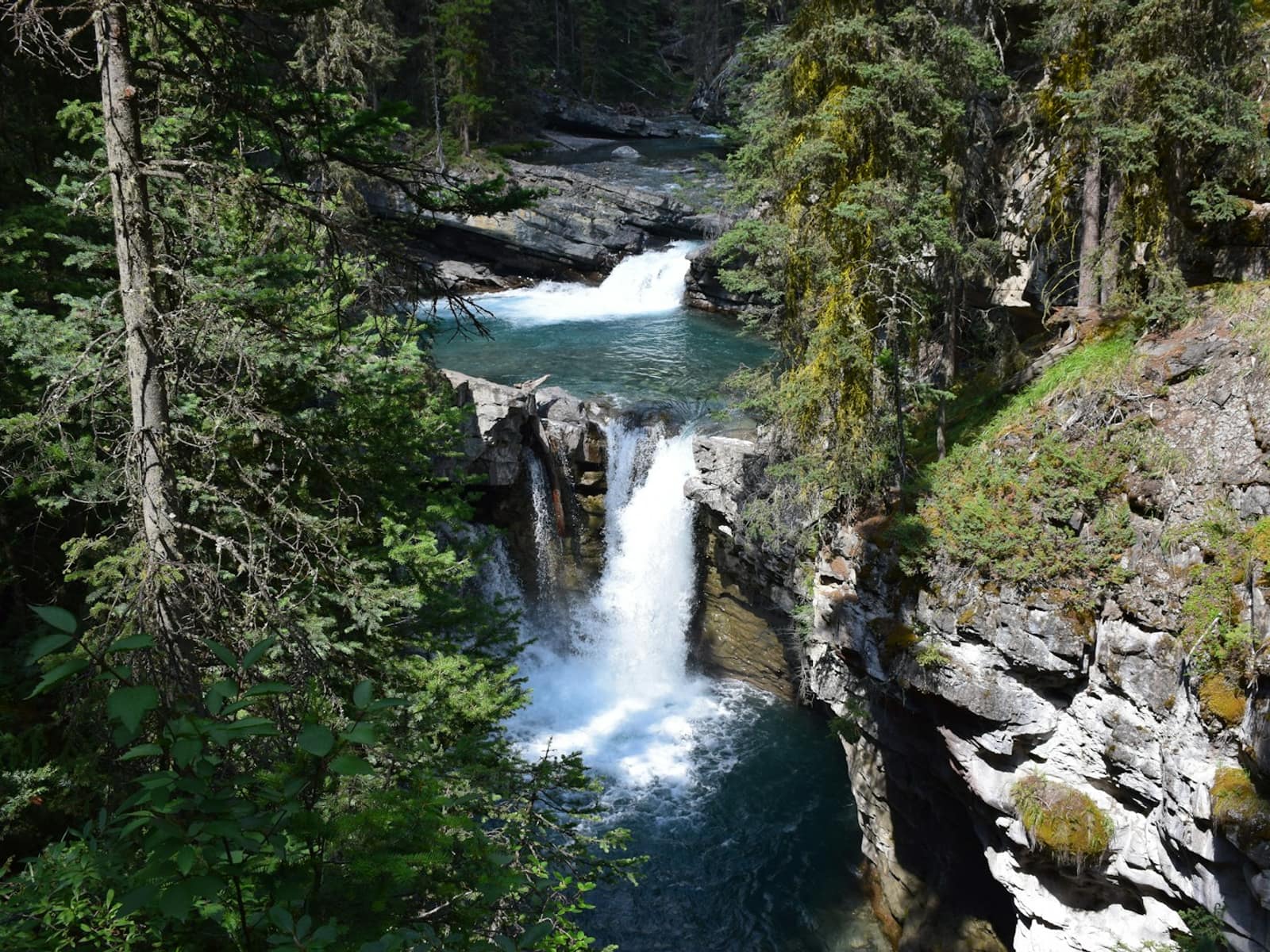 Tiered waterfalls dropping into turquoise pools between limestone canyon walls