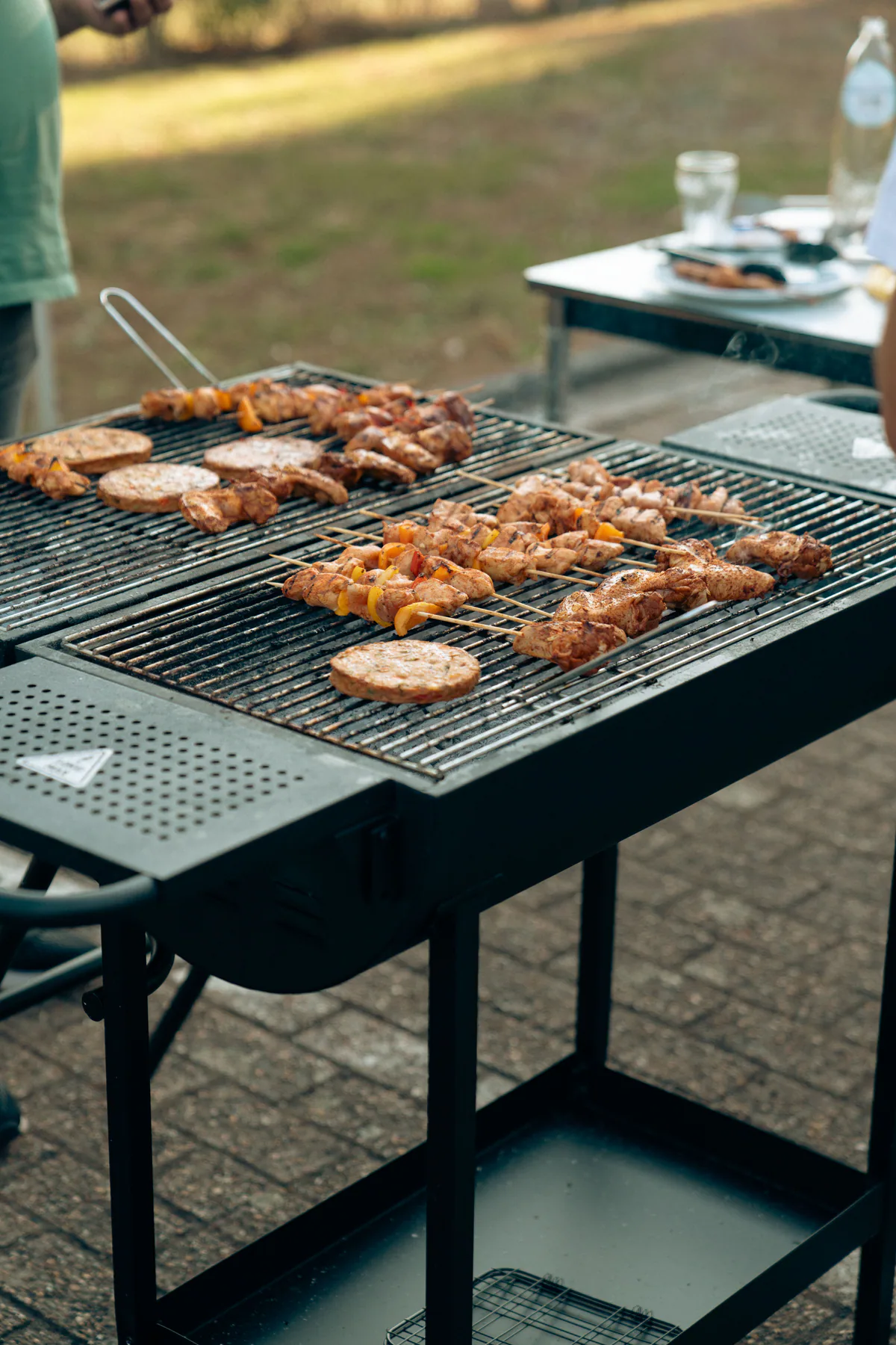 A cook tending chicken, skewers and other foods across a large outdoor grill