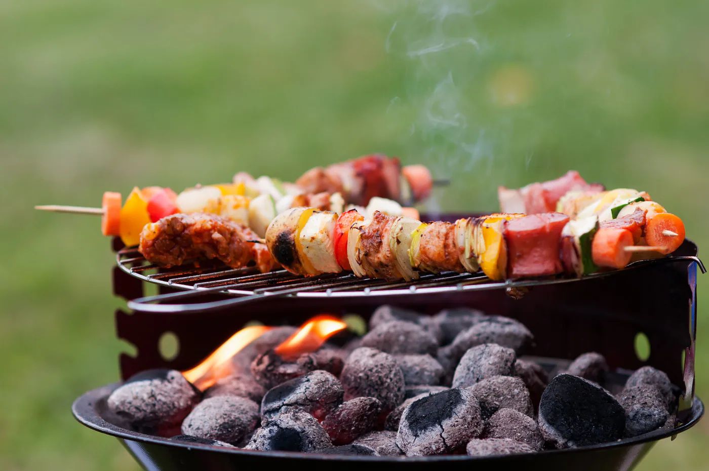 Colourful meat and vegetable skewers cooking on a small portable charcoal grill outdoors